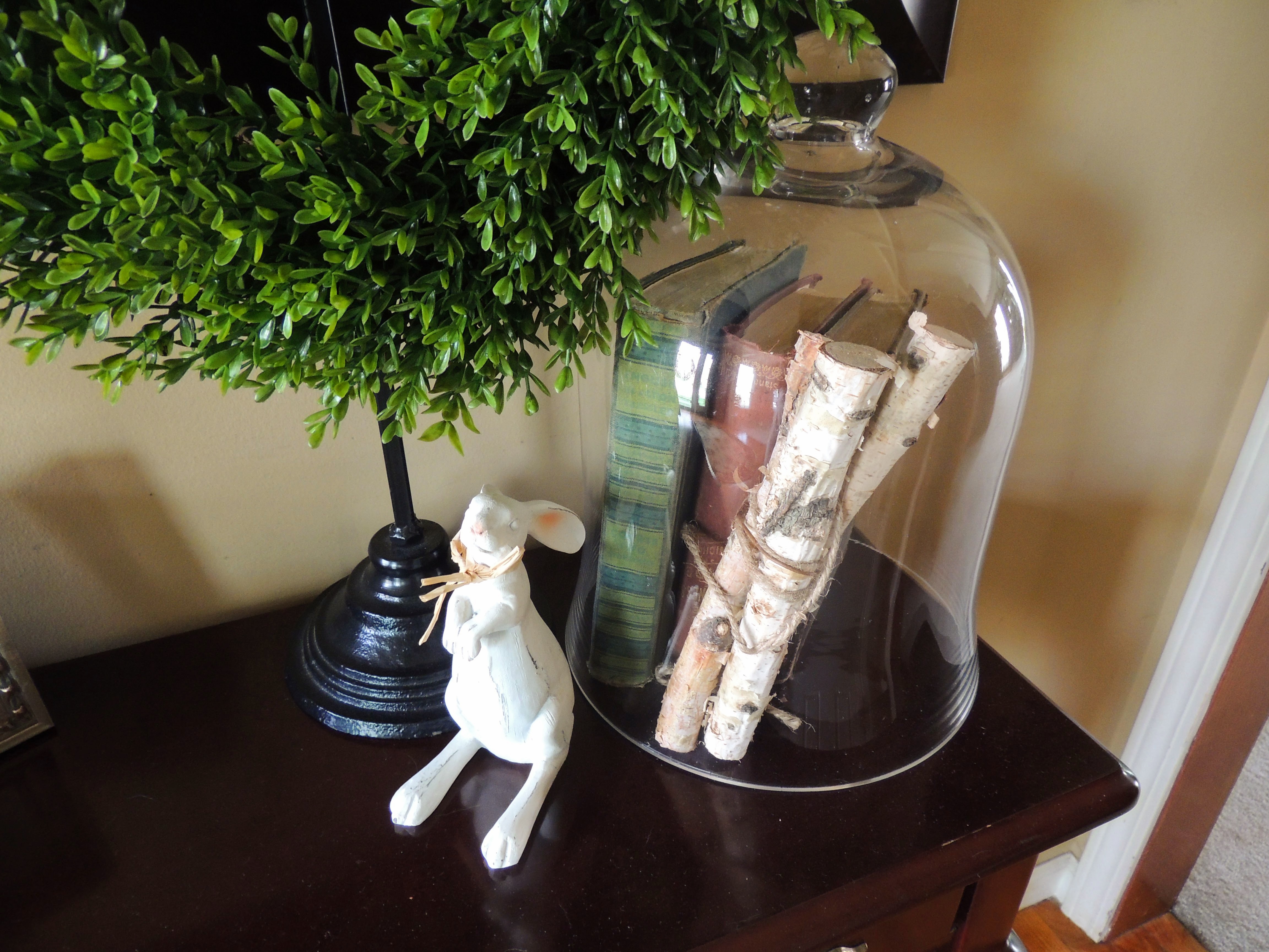 Weathered books and birch logs under glass cloche; wooden Easter bunny